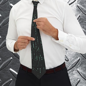 Pu&ograve; includere: Una cravatta nera con un motivo a matrice di caratteri verdi. La cravatta &egrave; indossata con una camicia bianca e pantaloni neri. La persona sta sistemando la cravatta.