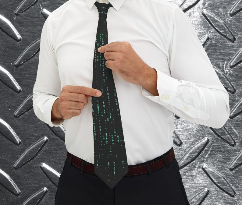 Pu&ograve; includere: Una cravatta nera con un motivo a matrice di caratteri verdi. La cravatta &egrave; indossata con una camicia bianca e pantaloni neri. La persona sta sistemando la cravatta.