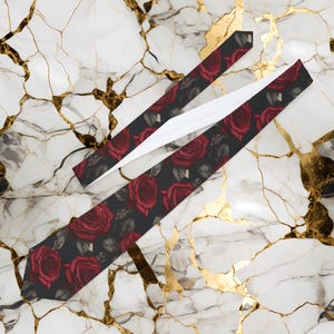 May include: Two neckties with a dark background and a pattern of red roses and gray leaves. The ties are laid out on a white and gold marble surface. The ties are a classic accessory.