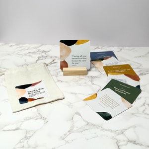 May include: A set of inspirational cards with the text "Ready, Set, Breathe" and various quotes. The cards have colorful abstract designs and are accompanied by a wooden block and a canvas bag.