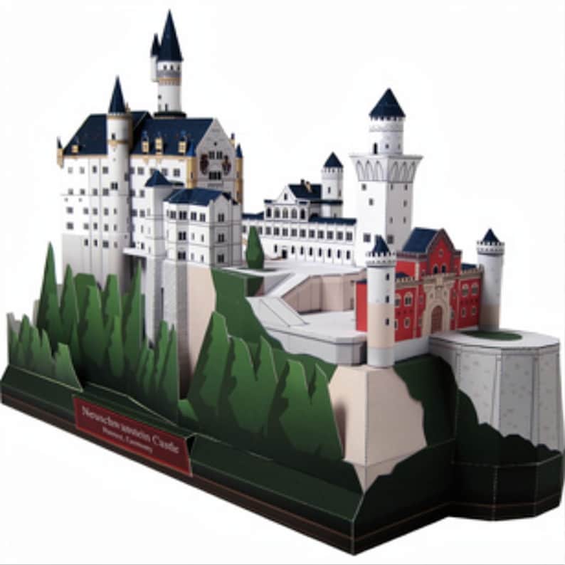 K&ouml;nnte beinhalten: Ein 3D-Papiermodell von Schloss Neuschwanstein mit wei&szlig;en W&auml;nden, blauen D&auml;chern und einem roten Torhausbereich. Das Bauwerk steht auf einem gr&uuml;nen Sockel, der einen H&uuml;gel mit stilisierten B&auml;umen darstellt. Ein rotes Etikett vorne tr&auml;gt die Aufschrift Neuschwanstein Castle, Fussen, Germany.