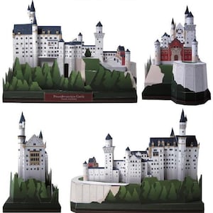 K&ouml;nnte beinhalten: Ein Papiermodellbausatz von Schloss Neuschwanstein mit wei&szlig;en Steinmauern, dunkelblauen D&auml;chern und mehreren T&uuml;rmen. Das Modell wird aus vier verschiedenen Blickwinkeln gezeigt und pr&auml;sentiert die architektonischen Details sowie die gr&uuml;ne Waldbasis.