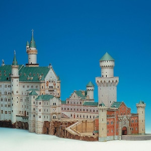 Puede incluir: Maqueta detallada del castillo de Neuschwanstein, con muros blancos, tejados verdes y múltiples torres. El modelo incluye detalles arquitectónicos como ventanas arqueadas y torretas, sobre un fondo azul brillante. La maqueta es una réplica en miniatura.