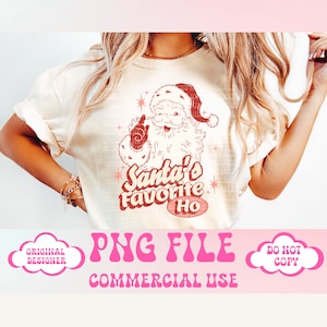 May include: A white t-shirt featuring a red and white illustration of Santa Claus with the text "Santa's Favourite Ho" in a retro font. The image is on a white background and the text is in a pink cloud.