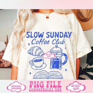 May include: A white t-shirt with a blue graphic design that says "Slow Sunday Coffee Club". The graphic also includes a coffee pot, a cup of coffee, a croissant, and an open book. The text "Do Not Copy" is in a pink cloud on the graphic.