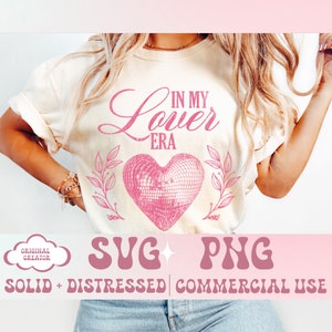 May include: Cream-colored t-shirt with the text "IN MY Lover ERA" in pink script above a pink disco ball heart design. The design is flanked by pink leafy branches. Below the design are the words "SVG PNG SOLID + DISTRESSED | COMMERCIAL USE".