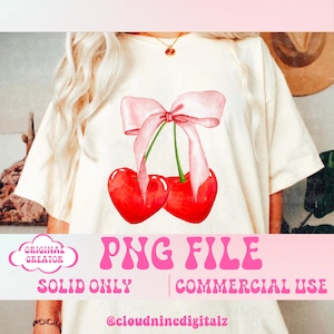 May include: Cream-colored t-shirt featuring a watercolor design of two red heart-shaped cherries tied with a pink bow. The text "PNG FILE" and "SOLID ONLY | COMMERCIAL USE" are displayed in pink. The creator's handle is also visible.