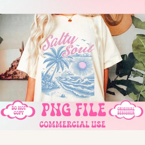 May include: A white t-shirt with a blue and pink graphic design of a palm tree, sun, and waves. The text "Salty Soul" is written in pink on the shirt. The shirt is being modeled by a person.