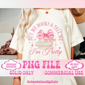 May include: A pink and white graphic design on a white t-shirt with the text "Buy me books & tell me I'm pretty". The design features a stack of books with a pink bow on top.