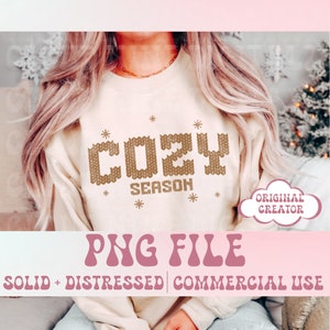 May include: A white sweatshirt featuring the text "Cozy Season" in gold knit-like lettering. The text is surrounded by small gold stars. The sweatshirt is being worn by a person with long blonde hair. The image also includes the text "PNG File" in a retro font and the text "Solid + Distressed | Commercial Use".