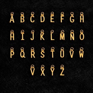 K&ouml;nnte beinhalten: Eine Sammlung von sechsundzwanzig einzelnen goldfarbenen Metall-Buchstabenanh&auml;ngern, die jeweils einen Gro&szlig;buchstaben von A bis Z zeigen. Jeder Buchstabenanh&auml;nger ist mit einem kleinen runden Biegering an der Oberseite zur Befestigung versehen.