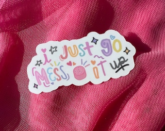 Puede incluir: Una pegatina blanca con el texto "I just go mess it up" en letras coloridas. El diseño incluye estrellas, corazones y una pequeña ilustración de pastel rosa. La pegatina está sobre un fondo de malla rosa.