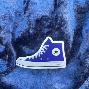 Op de afbeelding: Een paarse en witte sticker van een hoge sneaker met een witte ster aan de zijkant.