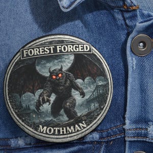 May include: Round button with the text "FOREST FORGED" at the top and "MOTHMAN" at the bottom. The button features a detailed illustration of a Mothman creature with red eyes, large wings, and a bridge in the background.