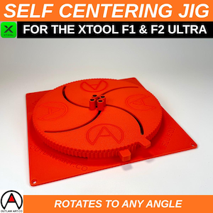 May include: An orange self-centering jig for the Xtool F1 & F2 Ultra. The jig has a circular design with the letter "A" in the center and the text "Rotates to any angle". The product is made by Outlaw Art.co.