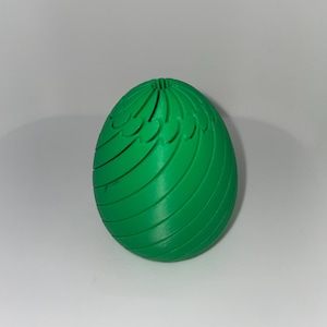 May include: A bright green, egg-shaped object with a textured surface. The egg has a series of curved, wing-like designs along its sides. The object is likely a decorative item or a unique piece of art.