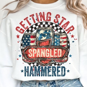 May include: White sweatshirt with a red, white, and blue graphic design. The graphic features three cans of beer with stars and stripes, a checkered background, and the text "Getting Star Spangled Hammered".