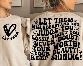 May include: A beige sweatshirt with a black heart and the text "Let them" on the front. The back of the sweatshirt has the text "Let them misunderstand you, judge you, gossip about you, never doubt your worth! Your beauty! Keep shining!" in a retro font.