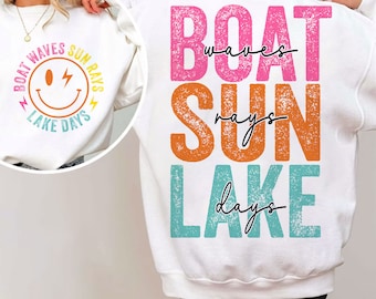 Op de afbeelding: Witte trui met een grafisch ontwerp op de rug dat "BOAT waves SUN rays LAKE days" zegt in kleurrijke, verweerde letters. De voorkant van de trui heeft een smiley met de tekst "BOAT waves SUN rays LAKE days" eromheen.