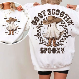 May include: White sweatshirt featuring a cartoon ghost wearing a cowboy hat and boots. The design includes bats and the text "Boot Scootin' Spooky". A smaller version of the design is on the front.