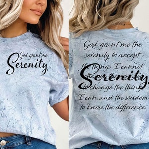 May include: A light blue t-shirt with a distressed, marbled effect. The shirt features a black graphic with the text "God, grant me Serenity" on the front and the text "God, grant me the serenity to accept the things I cannot change, Serenity to change the things I can, and the wisdom to know the difference." on the back.