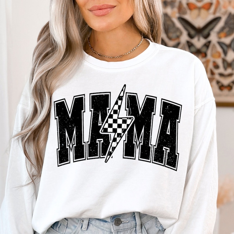 Puede incluir: Sudadera blanca de manga larga con un estampado gr&aacute;fico negro de la palabra "MAMA" en una fuente de estilo vintage con un rayo a cuadros en el centro.