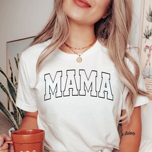 May include: White t-shirt with a black outline of the word "MAMA" in a collegiate font.