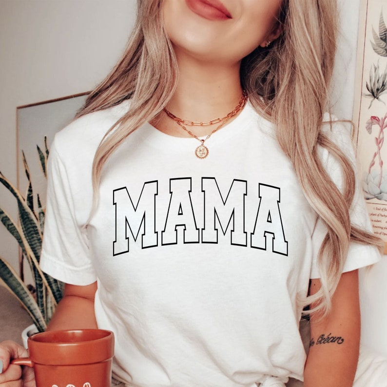 May include: White t-shirt with a black outline of the word "MAMA" in a collegiate font.