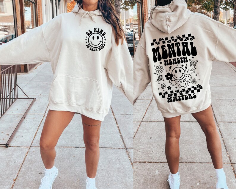 May include: A cream-colored hoodie with a black graphic on the front that says "Be Kind to Your Mind" with a smiley face. The back of the hoodie has a black graphic that says "Mental Health Matters" with smiley faces and flowers.
