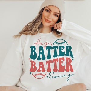 May include: White sweatshirt with a retro-style graphic design that says "Hey Batter Batter Swing" with a baseball graphic.