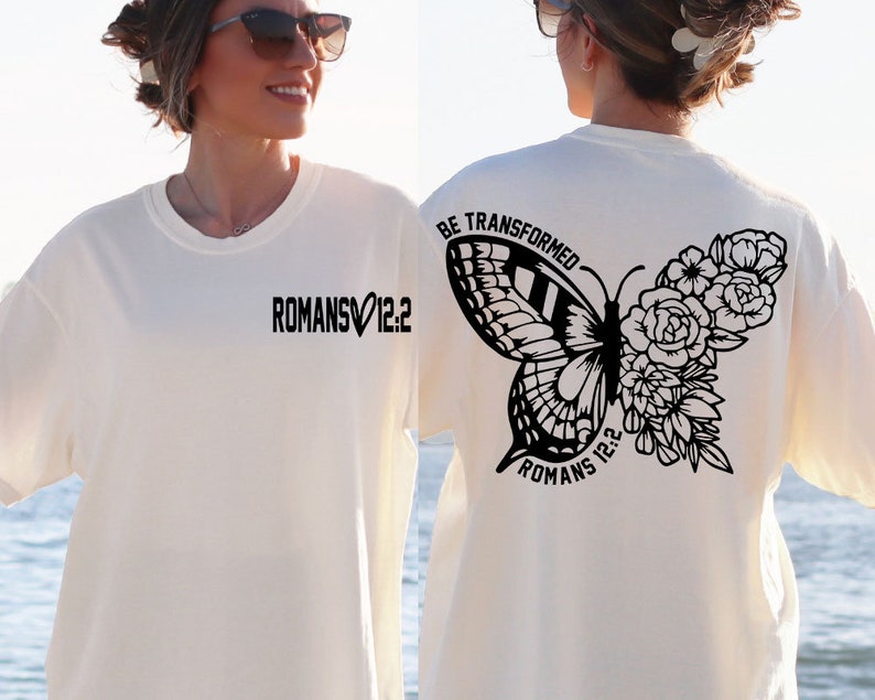 May include: White t-shirt with black text and a butterfly graphic on the back. The text reads "BE TRANSFORMED" and "ROMANS 12:2". The front of the shirt has the text "ROMANS 12:2" with a heart symbol.