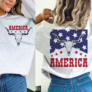 May include: Two gray sweatshirts with a skull and crossbones design and the word "AMERICA" printed on them. The skull and crossbones are in a red, white, and blue color scheme.