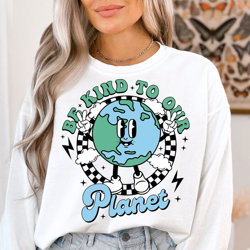 May include: White long-sleeve sweatshirt with a graphic of a cartoon Earth with a smiling face and the text "Be Kind To Our Planet" in a retro style.