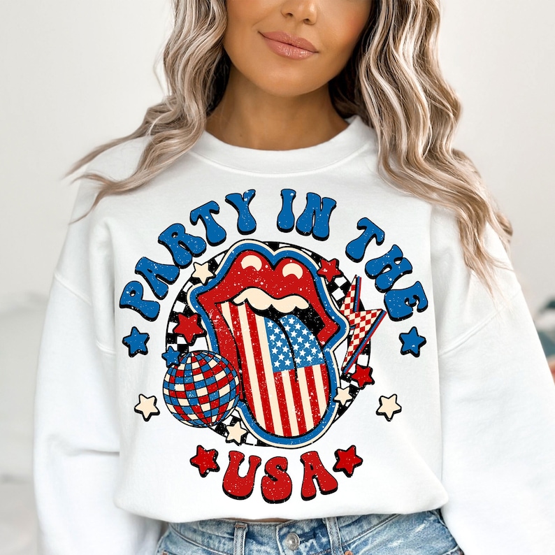 May include: White sweatshirt with a red, white, and blue graphic design. The graphic features a tongue with the American flag design, a disco ball, and the text "Party in the USA".
