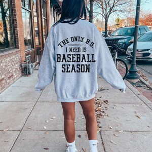 May include: A grey sweatshirt with the text "The only B.S. I need is baseball season" printed on the back. A baseball bat graphic is included in the text.