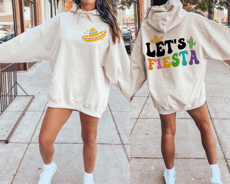May include: A cream-colored hoodie with a colorful "Let's Fiesta" graphic on the back and a sombrero graphic on the front. The hoodie has a drawstring hood and a kangaroo pocket.