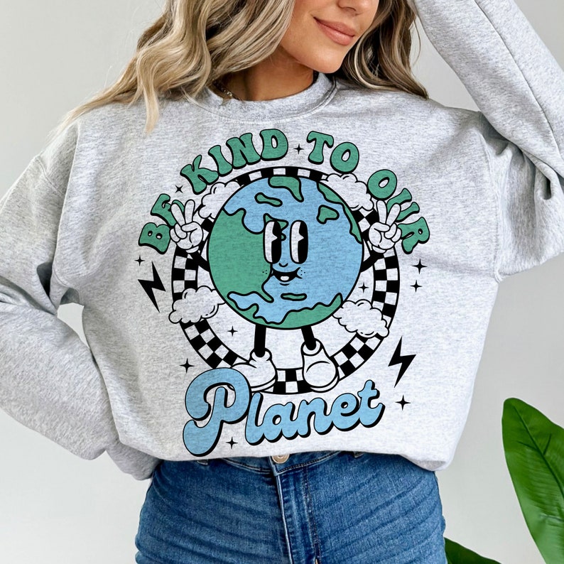 May include: Gray sweatshirt with a graphic of a smiling cartoon Earth holding up peace signs. The text "Be Kind To Our Planet" is written in a retro font around the Earth.