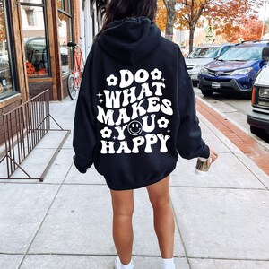 K&ouml;nnte beinhalten: Schwarzer Kapuzenpullover mit wei&szlig;em Text, der "Do what makes you happy" mit einem Smiley-Gesicht lautet.