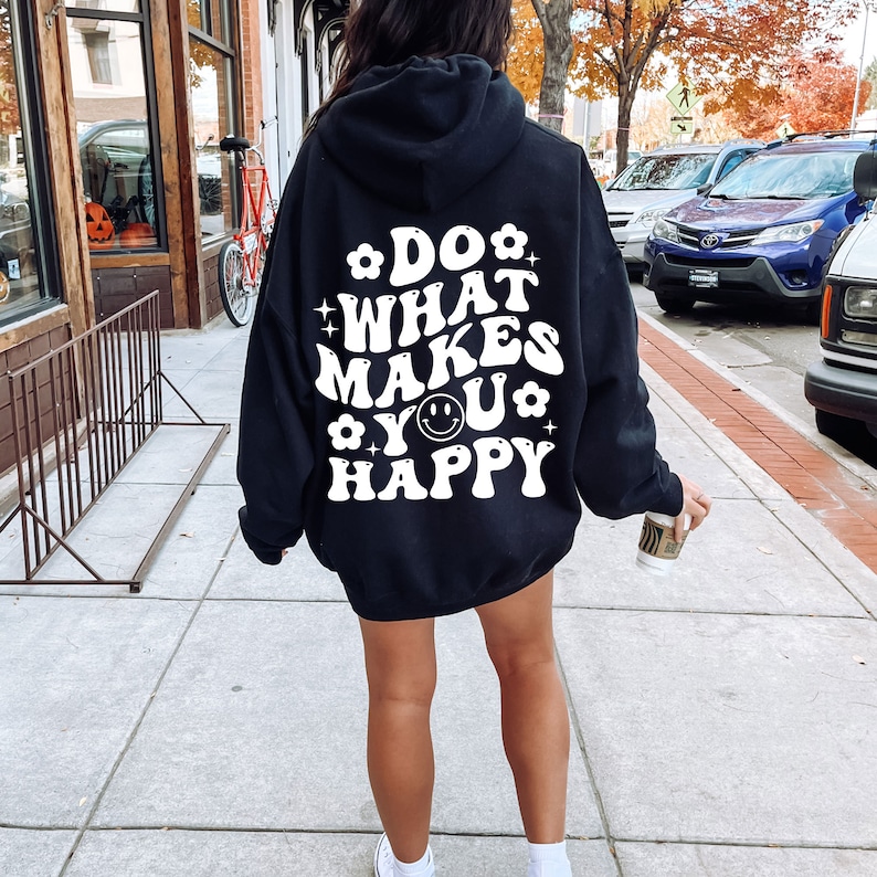 K&ouml;nnte beinhalten: Schwarzer Kapuzenpullover mit wei&szlig;em Text, der "Do what makes you happy" mit einem Smiley-Gesicht lautet.