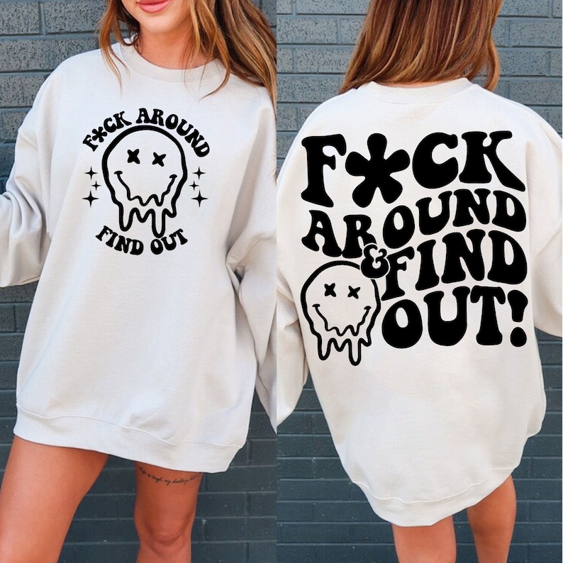May include: A white sweatshirt with a black graphic print on the front and back. The front graphic says "F*CK AROUND FIND OUT" with a dripping smiley face. The back graphic says "F*CK AROUND & FIND OUT!" with a dripping smiley face.