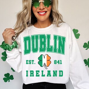 May include: White sweatshirt with green text that reads "DUBLIN EST. 841 IRELAND". A green shamrock with an orange and white center is between the words "EST." and "841".