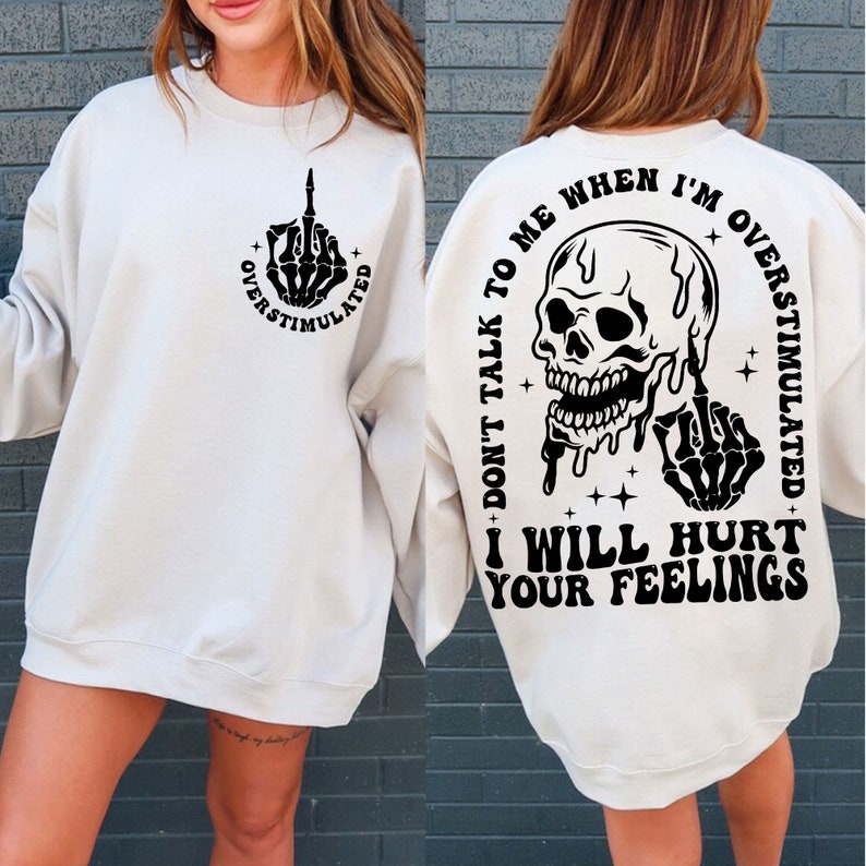 May include: White sweatshirt with a black skull and middle finger graphic on the back. The text reads "Don't talk to me when I'm overstimulated. I will hurt your feelings."