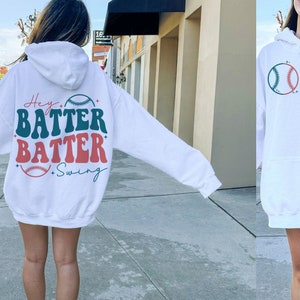 May include: White hooded sweatshirt with a green and red baseball graphic and the text "Hey Batter Batter Swing" on the back.