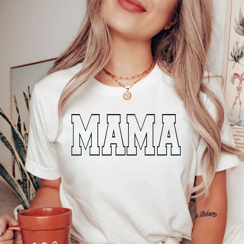 May include: White t-shirt with the word "MAMA" printed in black block letters.