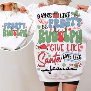 May include: White sweatshirt with a colorful Christmas-themed graphic. The design includes the words "Frosty Rudolph" and "Dance like Frosty, Give like Santa, Love like Jesus". Festive snowflakes and a Santa hat are also featured.