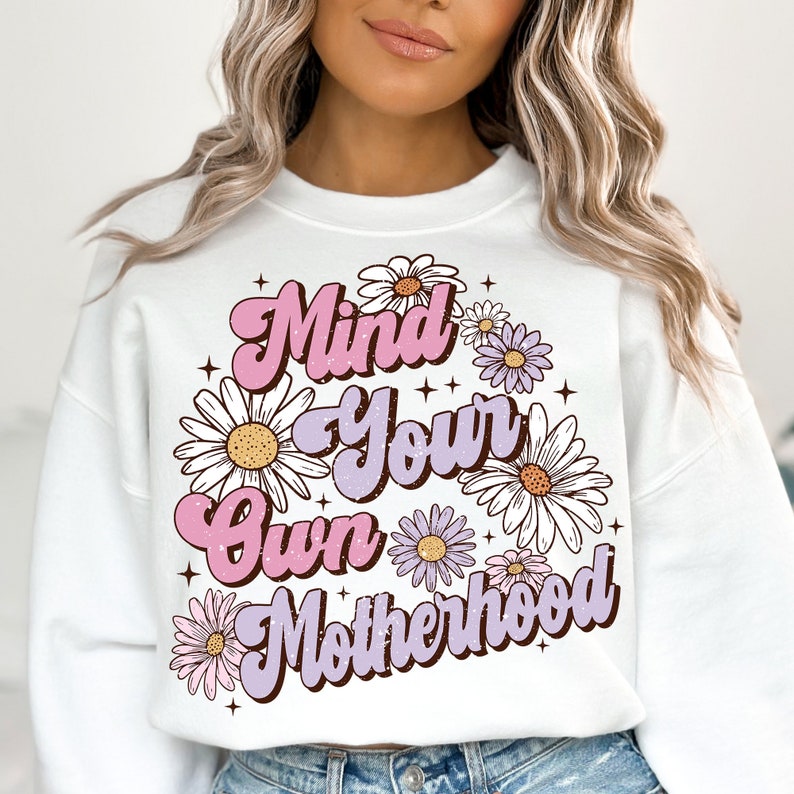 May include: White sweatshirt with a pink and purple graphic that says "Mind Your Own Motherhood" surrounded by white daisies.