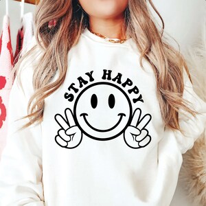 K&ouml;nnte beinhalten: Wei&szlig;er Pullover mit einem schwarzen Smiley und dem Text "STAY HAPPY" in Schwarz.