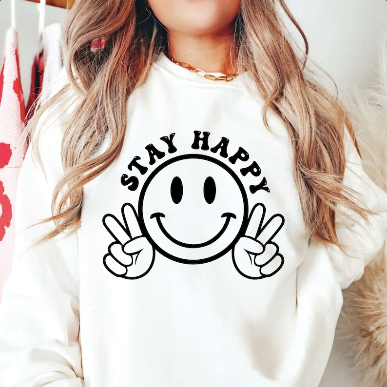 K&ouml;nnte beinhalten: Wei&szlig;er Pullover mit einem schwarzen Smiley und dem Text "STAY HAPPY" in Schwarz.