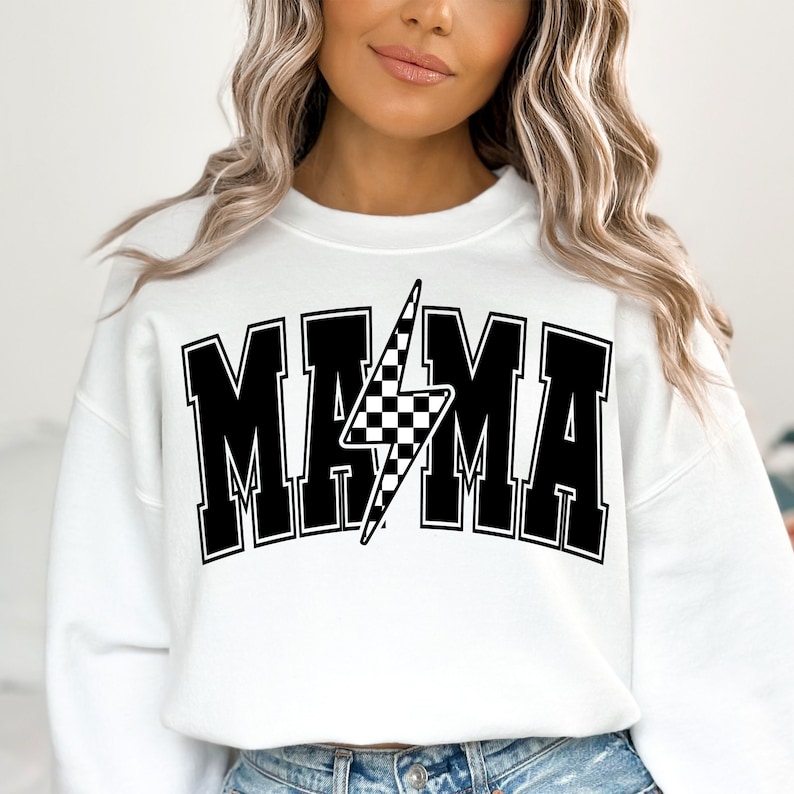 Puede incluir: Sudadera blanca con texto negro que dice "MAMA" con un rayo negro y blanco a cuadros en el medio.