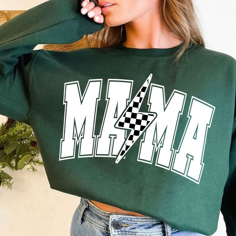 Puede incluir: Sudadera verde con un gr&aacute;fico blanco de la palabra "MAMA" con un rayo a cuadros en el medio.